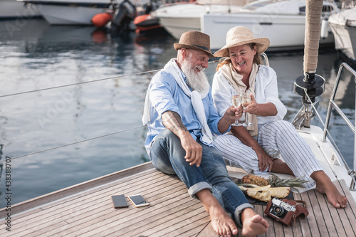 Senior couple cheering with champagne on sailboat during summer vacation - Focus on faces