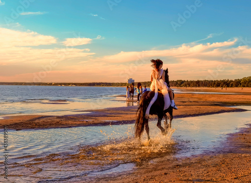 A young beautiful girl in a long dress rides a horse on the beach of the Gulf of Finland