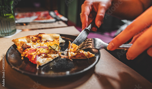 woman hands with knife and fork cutting pizza on table in cafe