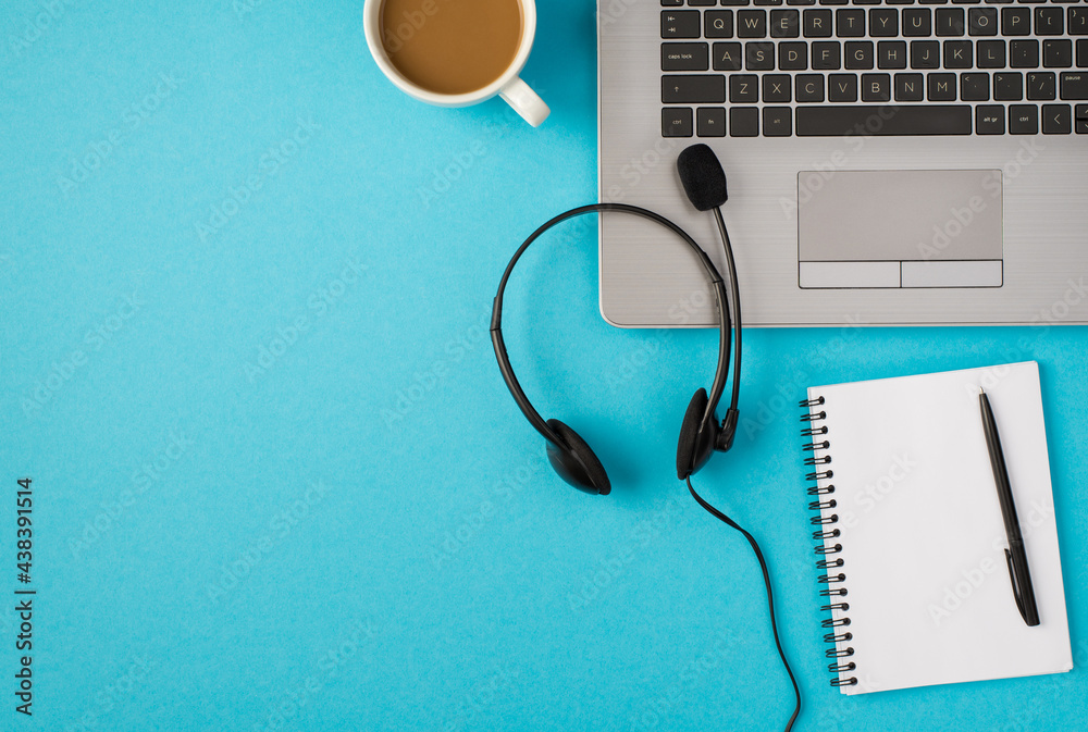 Top view photo of laptop headset with microphone cup of drink and pen on open reminder on isolated pastel blue background with blank space Top view photo of laptop headset with microphone cup of drink and pen on open reminder on isolated pastel blue background with blank space