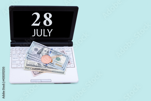 Laptop with the date of 28 july and cryptocurrency Bitcoin, dollars on a blue background. Buy or sell cryptocurrency. Stock market concept.