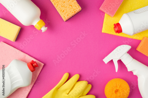 Top view photo of scouring pads viscose rags rubber gloves and white detergent bottles without label on isolated pink background with copyspace