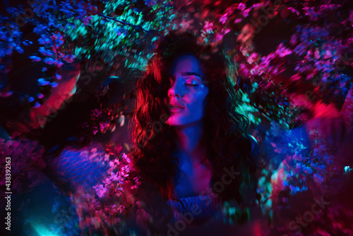 A fantastic shot of a girl in flowers with neon multicolored light and phantasmagoria. The concept of fantasy  fairy tales  magic and fairies.