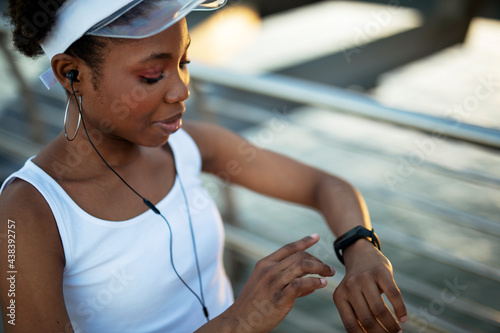 Young african woman training outdoors. Female runner using smart watch..