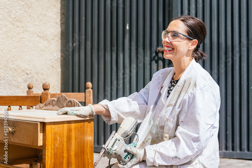 very smiling latin woman working in her carpentry business and holding a sander in her hand. small carpentry and furniture restoration business. photo