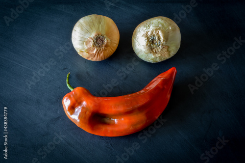 Two golden onions and one red sweet pointed pepper on a blackboard making an happy face close up