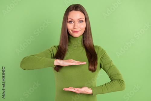 Photo of positive charming pretty young woman hold hands empty space object isolated on green color background photo