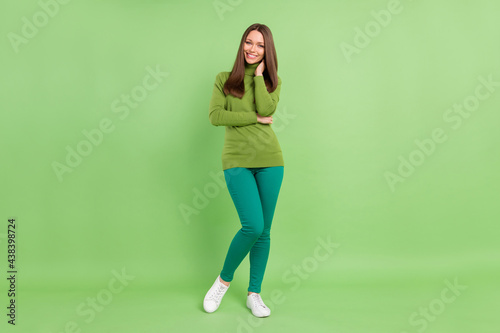 Full size photo of cheerful young happy lady hold hands face good mood smile isolated on green color background © deagreez