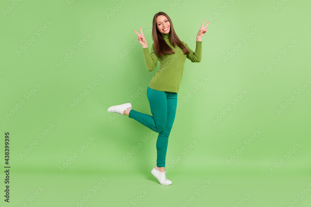 Full size photo of positive nice pretty young woman make v-signs smile cool isolated on green color background Full size photo of positive nice pretty young woman make v-signs smile cool isolated on green color background