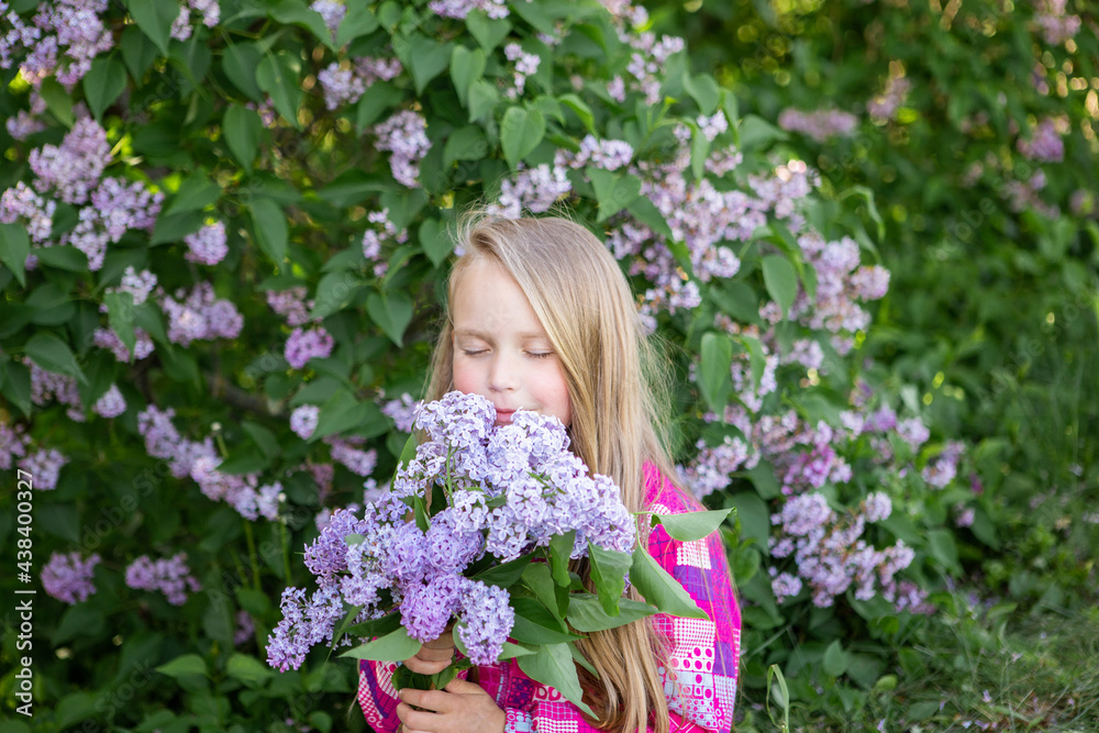 Cute blonde girl enjoys the scent of lilacs. City walk. Spring and summer