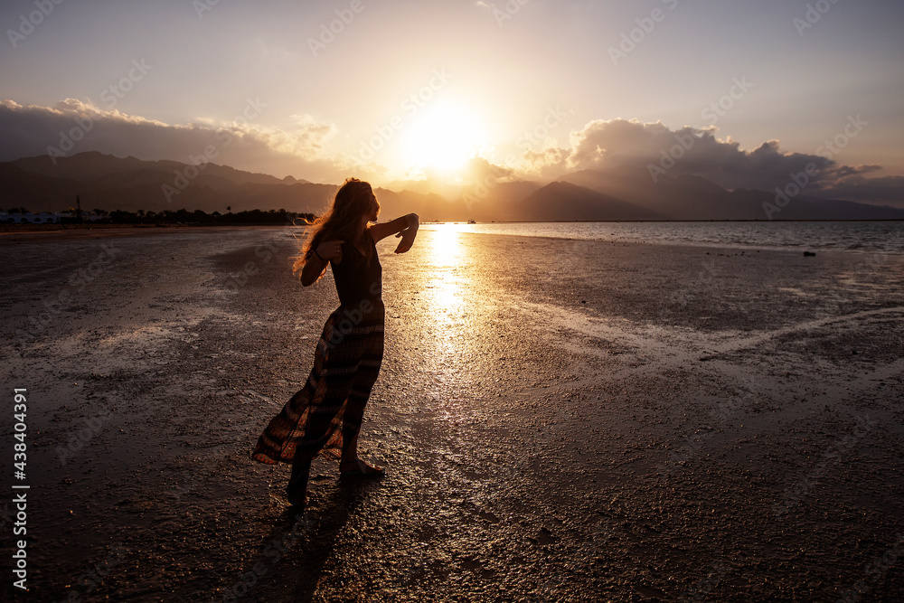 Fototapeta premium Beautiful woman dancing by the sea at sunset