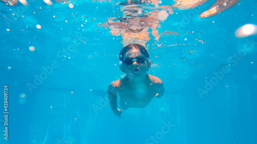 Happy young boy swim and dive underwater, kid breaststroke with fun in pool. Active healthy lifestyle, water sport activity and lessons with parents on summer family vacation with child.