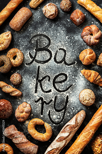 ‘Bakery’ sign on flour and various kinds of breadstuff around on black background
