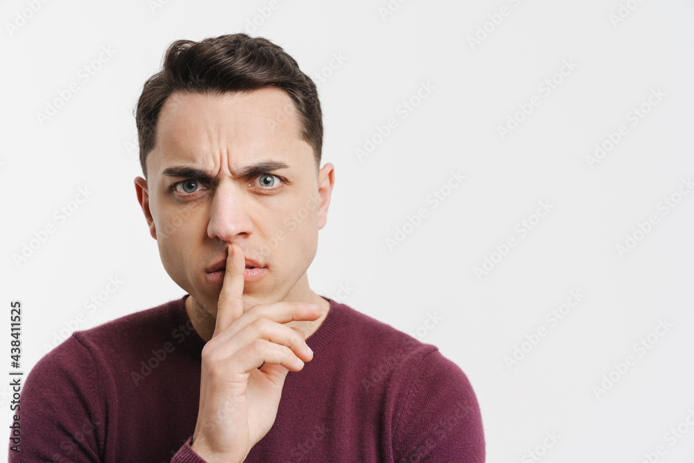 Young white man frowning and showing silence gesture at camera Young white man frowning and showing silence gesture at camera