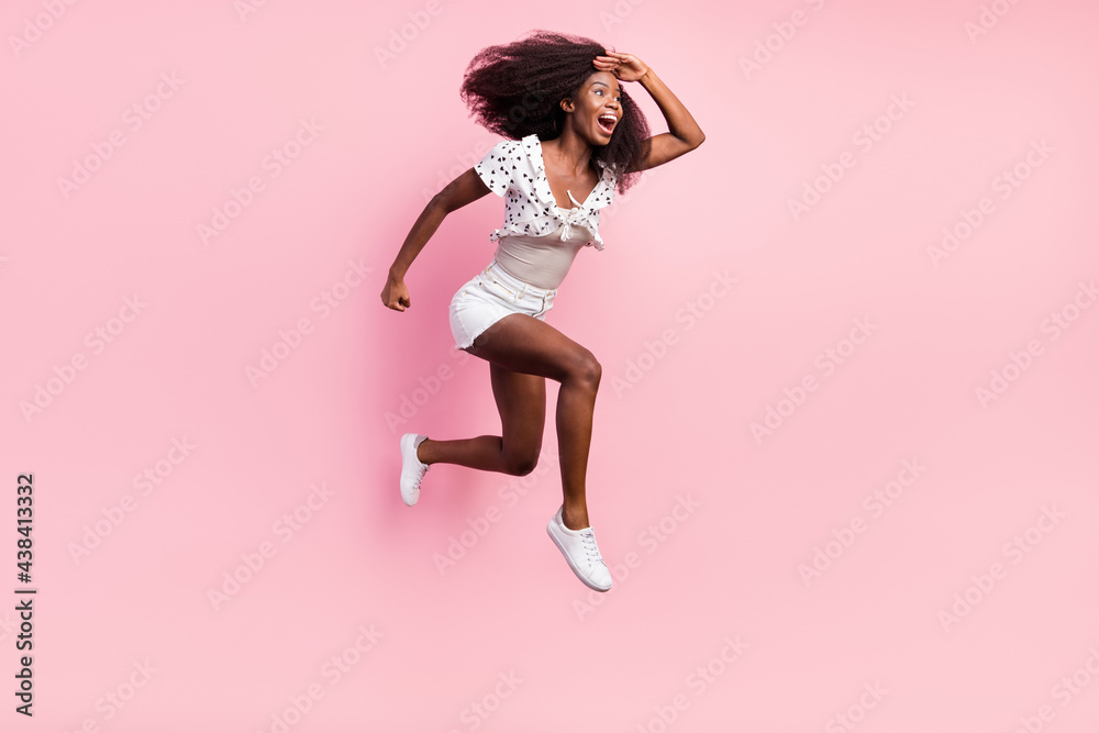 Full size photo of funky excited crazy african girl jumping look forward ahead in copyspace isolated on pink color background Full size photo of funky excited crazy african girl jumping look forward ahead in copyspace isolated on pink color background