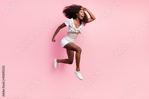 Full size photo of funky excited crazy african girl jumping look forward ahead in copyspace isolated on pink color background