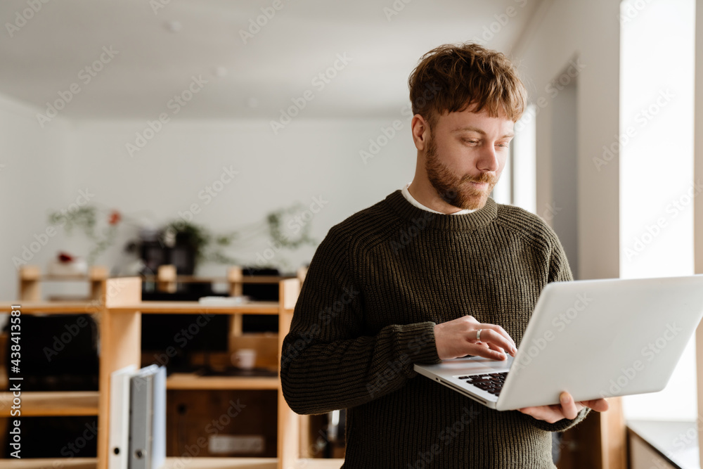 Young ginger man working with laptop while standing in office Young ginger man working with laptop while standing in office