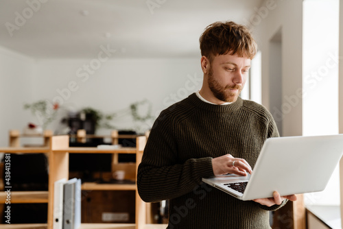 Young ginger man working with laptop while standing in office