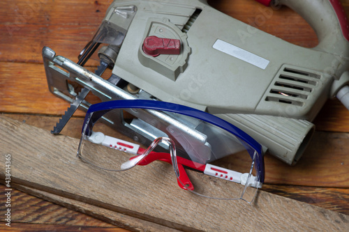 Jigsaw and safety goggles on a wooden background. Electric woodworking tool