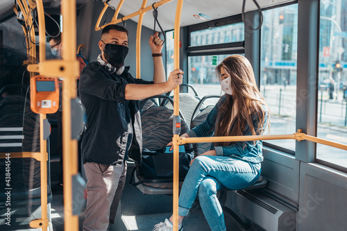 Young passengers in the bus wearing protective mask and using smartphone