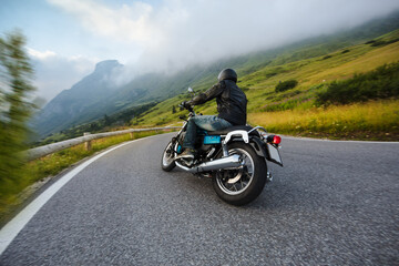 Motorcycle driver riding in Alpine landscape. Lifestyle photo with motion blur effect and copyspace.