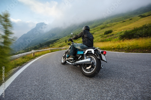 Motorcycle driver riding in Alpine landscape. Lifestyle photo with motion blur effect and copyspace.