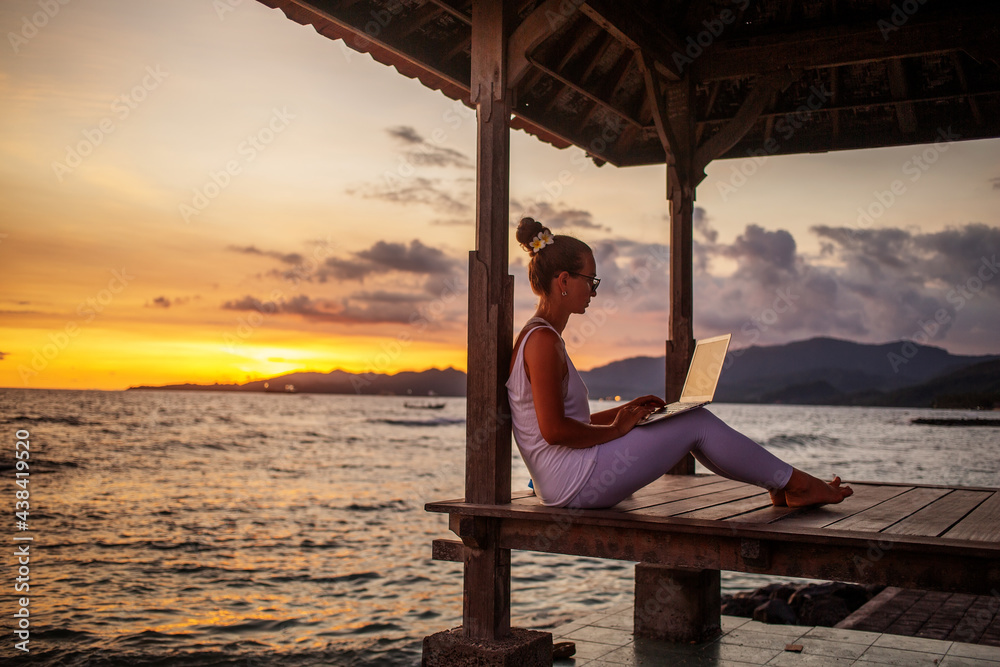Woman by the ocean working on a laptop