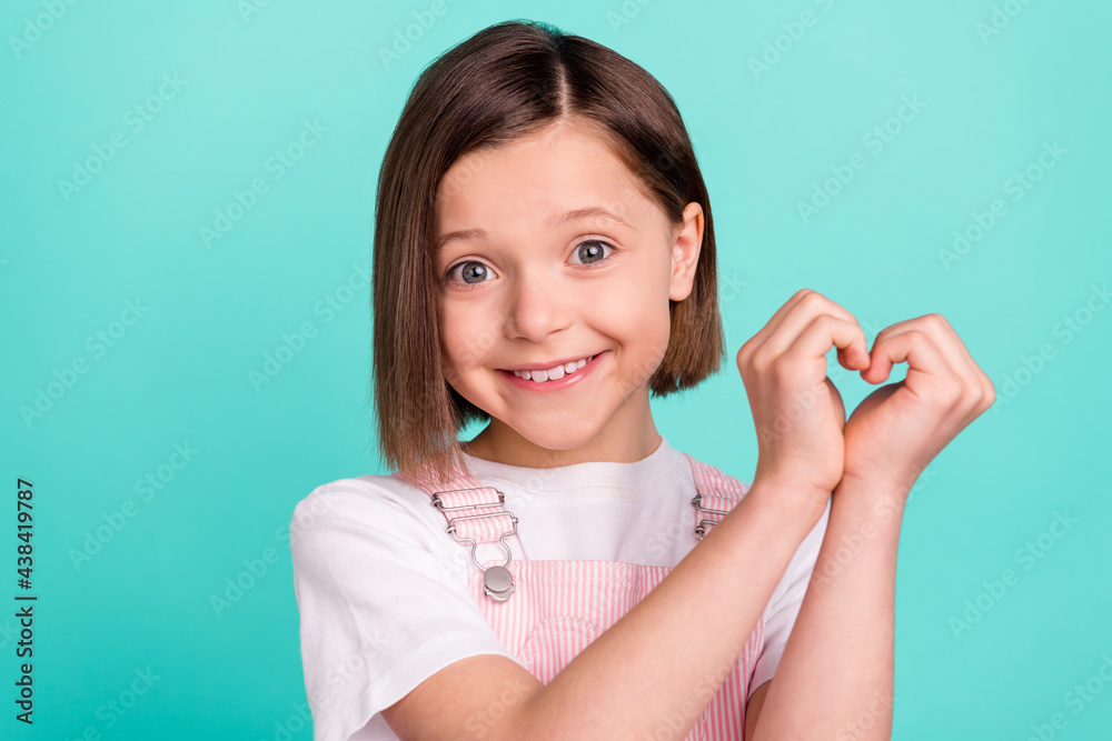 Photo of pretty cute schoolgirl dressed pink overall showing arms heart smiling isolated turquoise color background Photo of pretty cute schoolgirl dressed pink overall showing arms heart smiling isolated turquoise color background