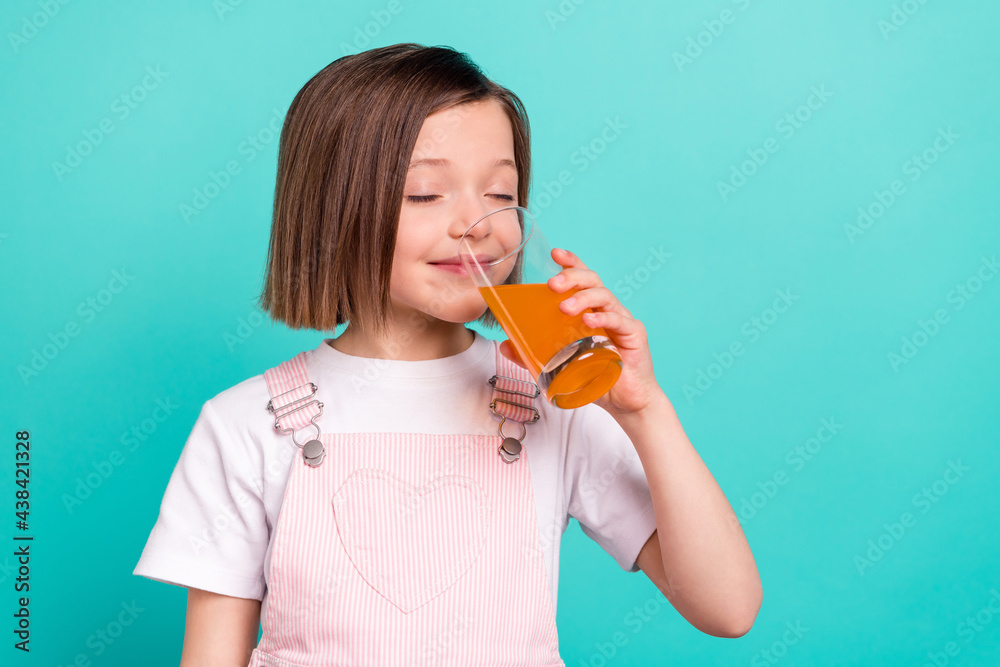 Photo of charming dreamy schoolgirl dressed pink overall enjoying glass of juice empty space smiling isolated turquoise color background Photo of charming dreamy schoolgirl dressed pink overall enjoying glass of juice empty space smiling isolated turquoise color background