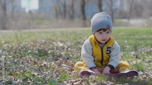 Spring walk with the kid in the park. Happy healthy baby sitting on tarve in the park in spring. Walking with the child in the fresh air. photo