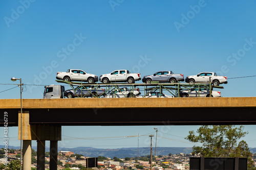 Um caminhão cegonha cheio de carros passando sobre um viaduto com céu azul ao fundo. photo