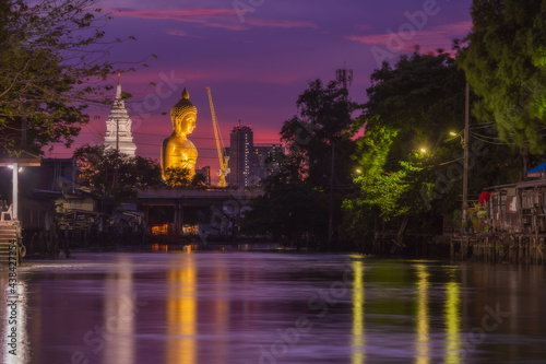 Big golden buddha statue under construction at Wat Paknam Bhasicharoen temple at Twilight time, viewed from Klong Dan, Bangkok, thailand