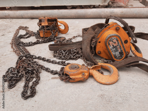 orange hook with sling belt and chain block or chain hoist which is placed on a cement floor, usually used for lifting in factories, with a maximum load specification of 2 tons