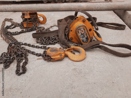 orange hook with sling belt and chain block or chain hoist which is placed on a cement floor, usually used for lifting in factories, with a maximum load specification of 2 tons