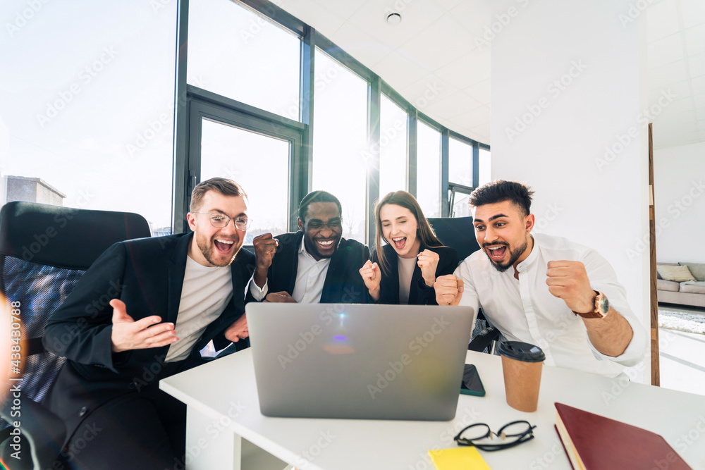 Team of business partners sit in office in front of a laptop and rejoice of the victory