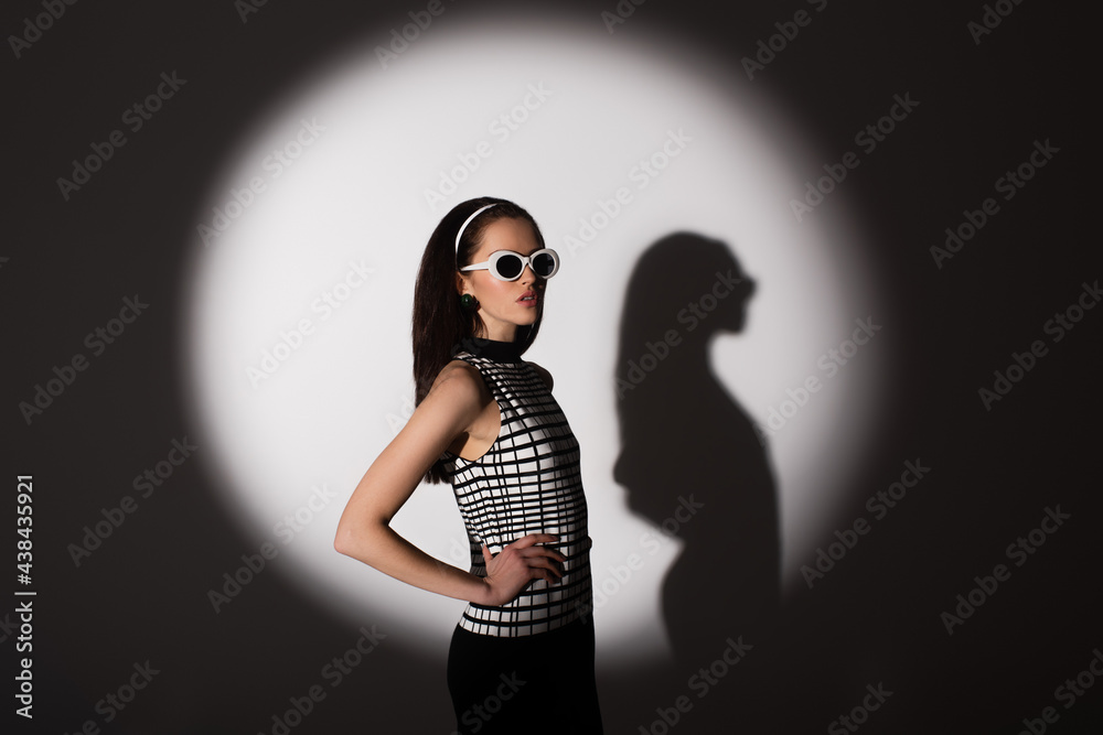 lighting on stylish model in retro sunglasses posing with hand on hip on grey. lighting on stylish model in retro sunglasses posing with hand on hip on grey.
