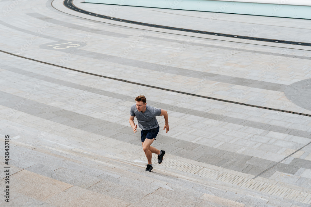 Young athlete man runner running up and down on city stairs in summer on morning run, background urban city street. Sports training. Fitness cardio workout in fresh air, walk outside.