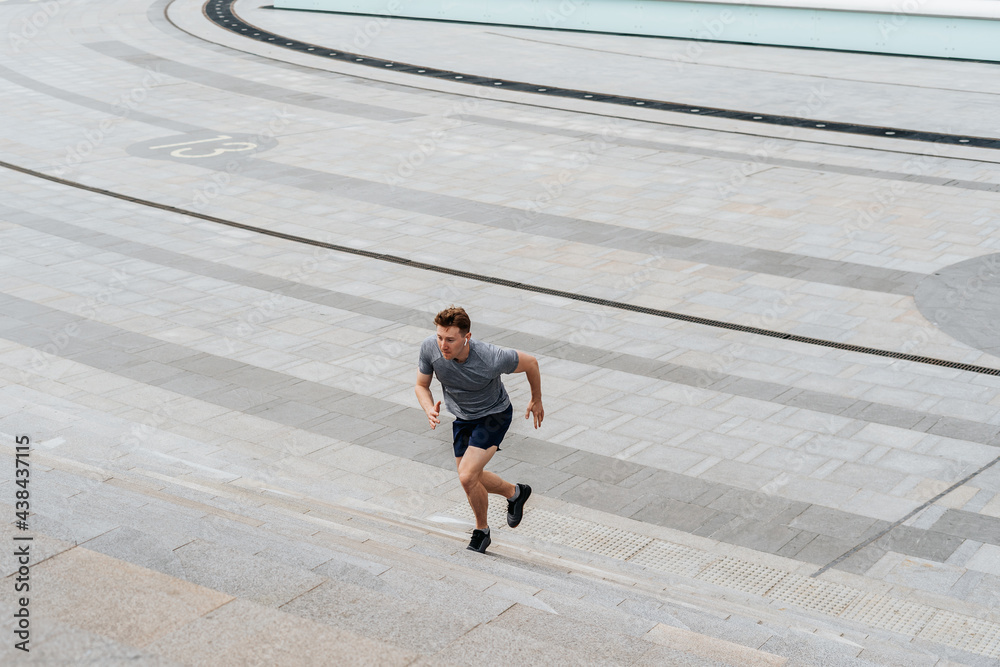 Young athlete man runner running up and down on city stairs in summer on morning run, background urban city street. Sports training. Fitness cardio workout in fresh air, walk outside. Young athlete man runner running up and down on city stairs in summer on morning run, background urban city street. Sports training. Fitness cardio workout in fresh air, walk outside.
