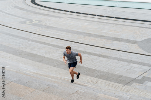 Young athlete man runner running up and down on city stairs in summer on morning run, background urban city street. Sports training. Fitness cardio workout in fresh air, walk outside.