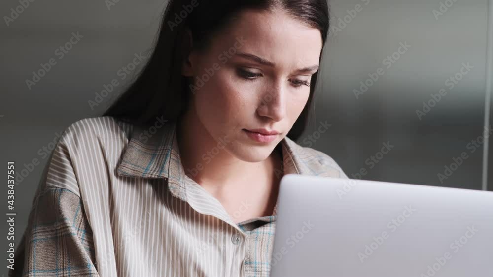 A close-up view of a thinking business woman wearing shirt is using her laptop then looking to the side sitting in the office A close-up view of a thinking business woman wearing shirt is using her laptop then looking to the side sitting in the office