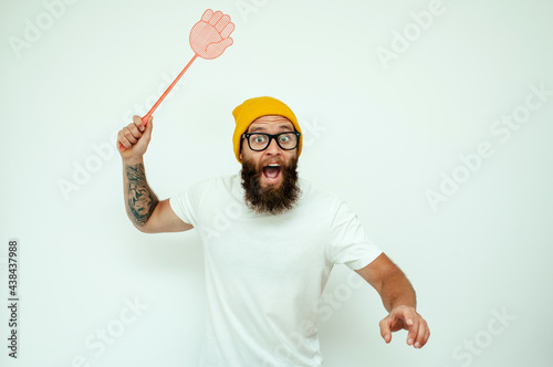 Young caucasian hipster man holding a fly swatter wanting to kill annoying mosquito or a fly.