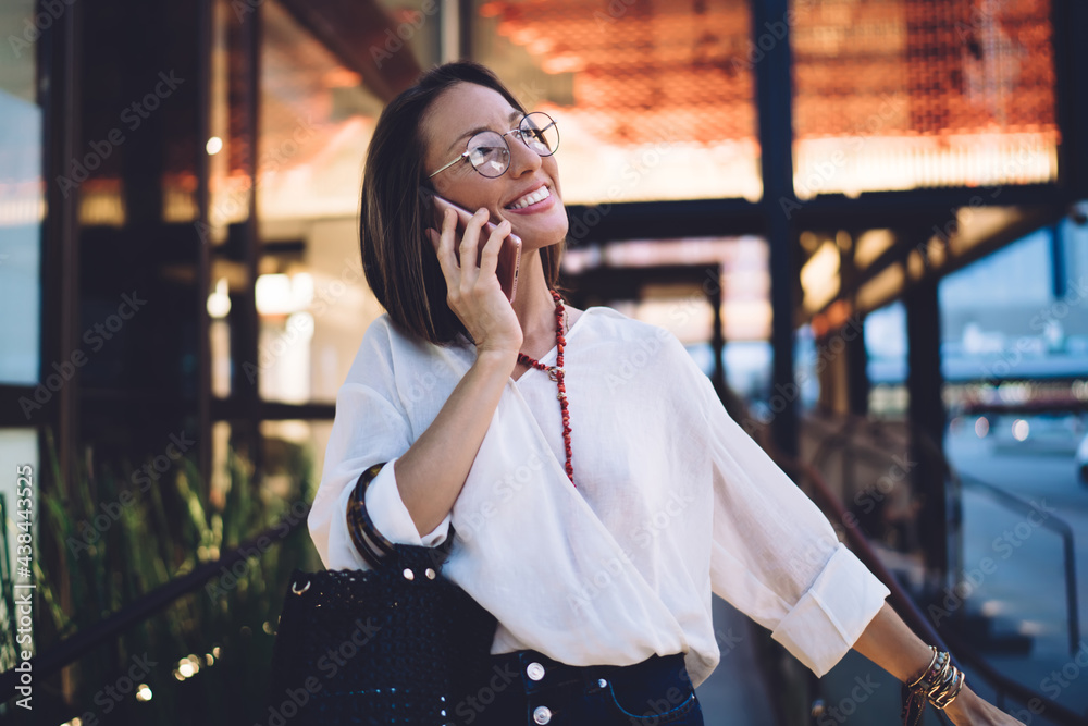Fototapeta premium Cheerful adult woman talking on smartphone on terrace