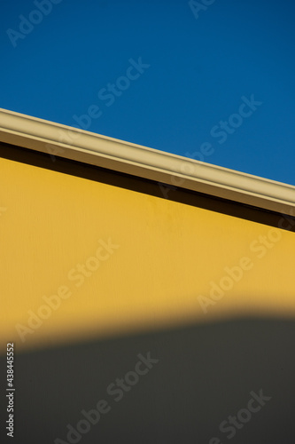 Yellow wall with a shadow on it and a blue sky