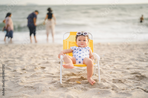 baby in white dress and sunglasses sit on the chair beach yellow color with smile happy and relaxing and the wind blows in evening time and beautiful sunset light at the beach