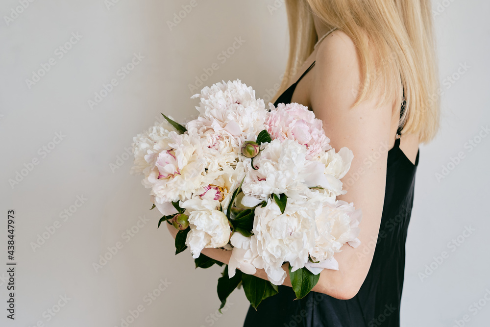 Naklejka premium A rich bouquet with peonies in the hands of a girl on a light background. Romantic festive bouquet. Fresh floral. A holiday gift. Beautiful white flowers. The florist girl gathered a bouquet