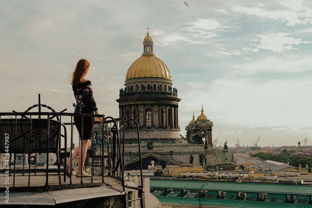 a red-haired girl walks on the roofs of St. Petersburg on the background of the Iskakevsky Cathedral