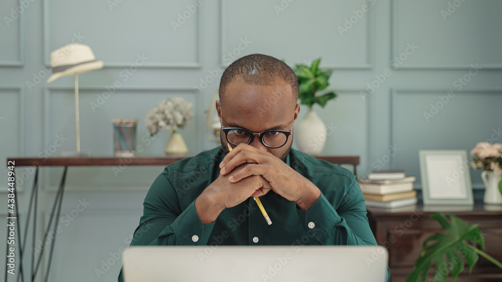 young african American man is thinking in front of a laptop.