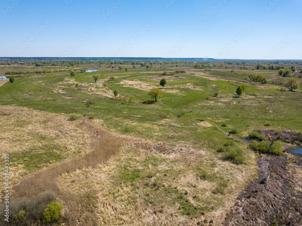 Green meadows on the outskirts of the city in spring. Aerial drone view.