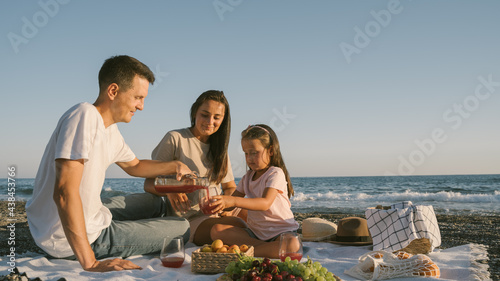 Family spending time together outdoor. Summer leisure concept with copyspace. Picnic lunch with fruits by the seaside. Happy people eating healthy food and sitting on blanket on the beach.