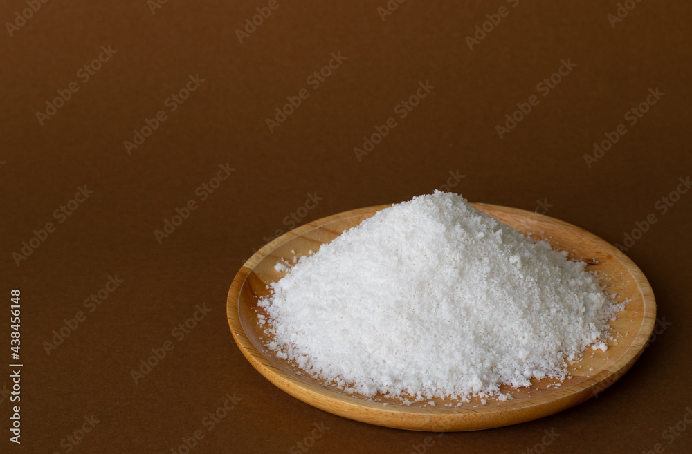 Coconut powder or dried coconut shredded on wood tray, brown background. Copy space.